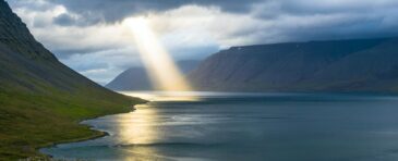 sun reflection on calm water near green mountains